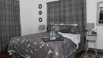 Ein Schlafzimmer mit einem Bett, Vorhängen, einem Nachttisch mit Lampe und einer kleinen Pflanze.