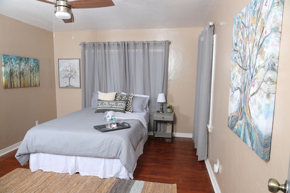 A bedroom with a bed, a nightstand, a ceiling fan, and artwork on the walls.