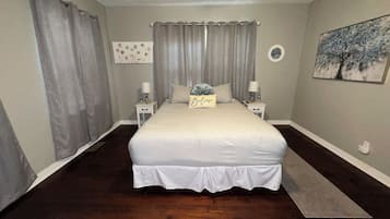 A bedroom with a large bed, two bedside tables with lamps, a nightstand, a wall clock, and a painting.