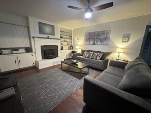 Uma sala de estar com lareira, sofá, mesa de centro e ventilador de teto.