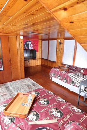 Una stanza con soffitto a falde, pareti in legno, un letto con copriletto decorato, un tavolino con vassoio e una televisione sullo sfondo.