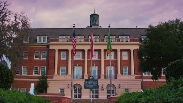 A historic building with a central entrance, multiple windows, and a flagpole with flags.