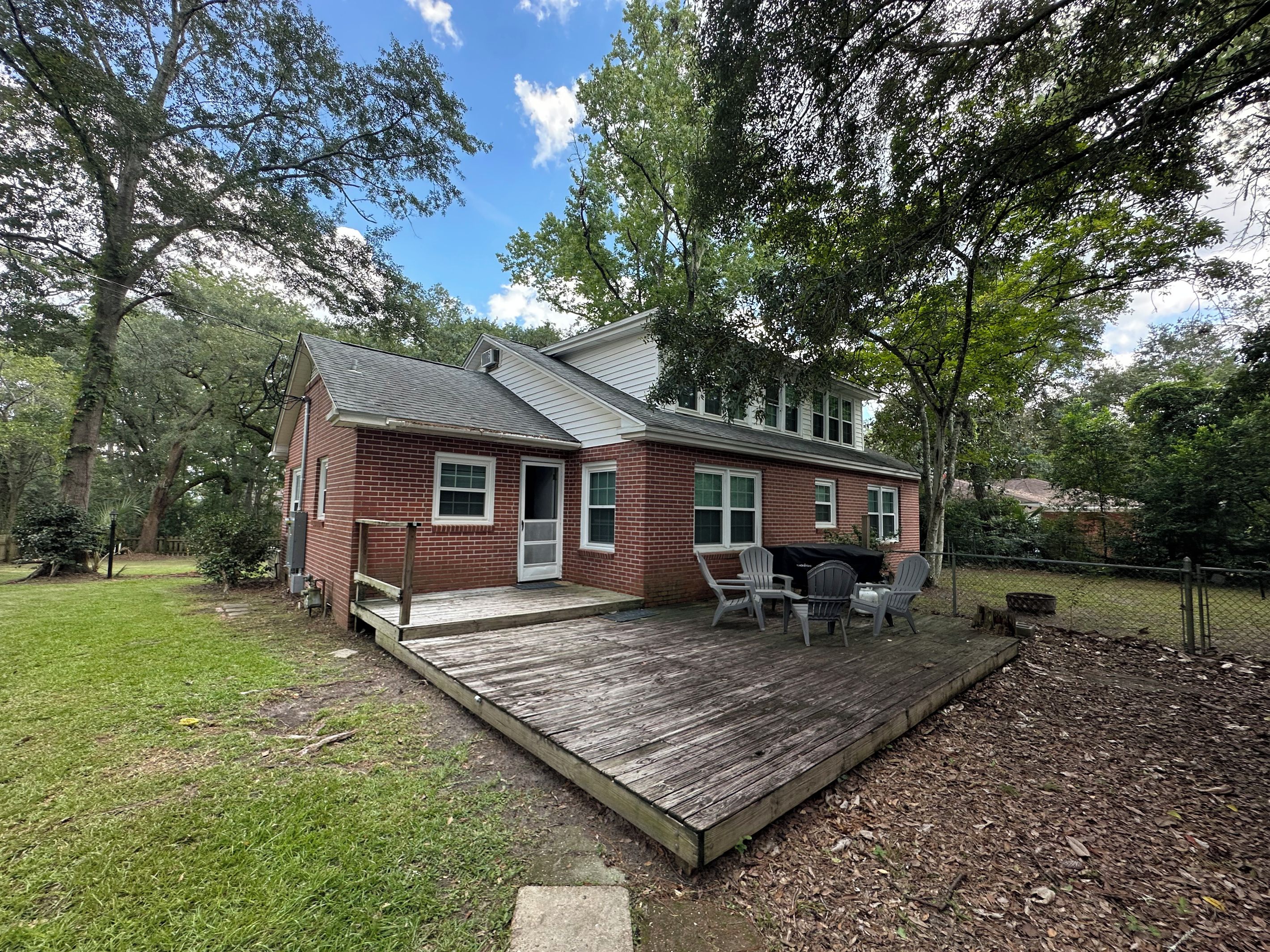 A two-story brick house with a deck, a barbecue grill, and a fenced yard.