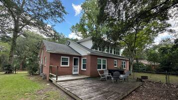 A two-story brick house with a deck, a barbecue grill, and a fenced yard.
