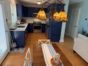 A modern kitchen with dark blue cabinets, stainless steel appliances, and a wooden dining table with a glass centerpiece.