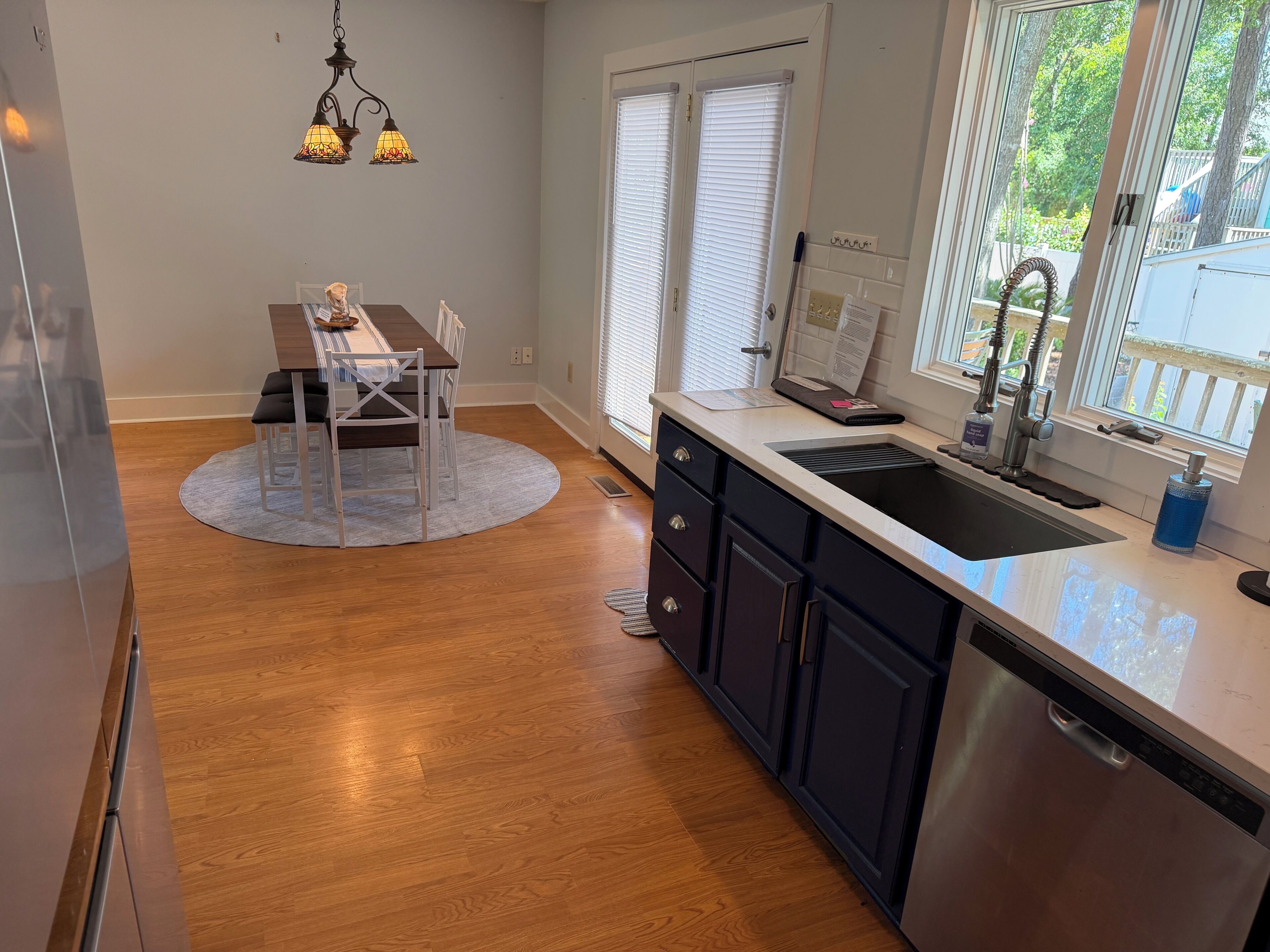 A kitchen with a stainless steel dishwasher, a sink with a faucet, and a window with blinds.