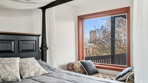 A bedroom with a large window, a bed with grey bedding, and a floral-patterned chair. - Beautiful Hillside Home with Incredible City Views!! Great Location and Privacy! (Pittsburgh)