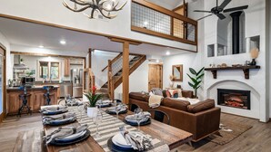 A spacious living area with a high ceiling, a fireplace, and a dining table set for a meal.