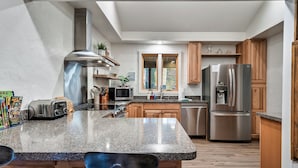 A modern kitchen with granite countertops, stainless steel appliances, wooden cabinets, and a window with curtains.