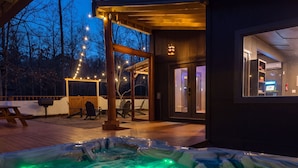 A hot tub area with a wooden deck, outdoor seating, and string lights.