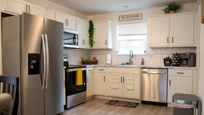 Una cocina moderna con electrodomésticos de acero inoxidable, armarios blancos y una ventana con persianas.