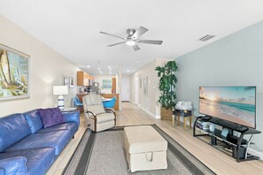A modern living room with a blue leather sofa, a beige armchair, a television, and a ceiling fan. - Fall into Autumn with nightly sunsets at this beautiful beachside unit! (Bradenton Beach)