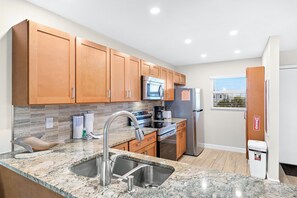 A modern kitchen with wooden cabinets, stainless steel appliances, and a granite countertop.