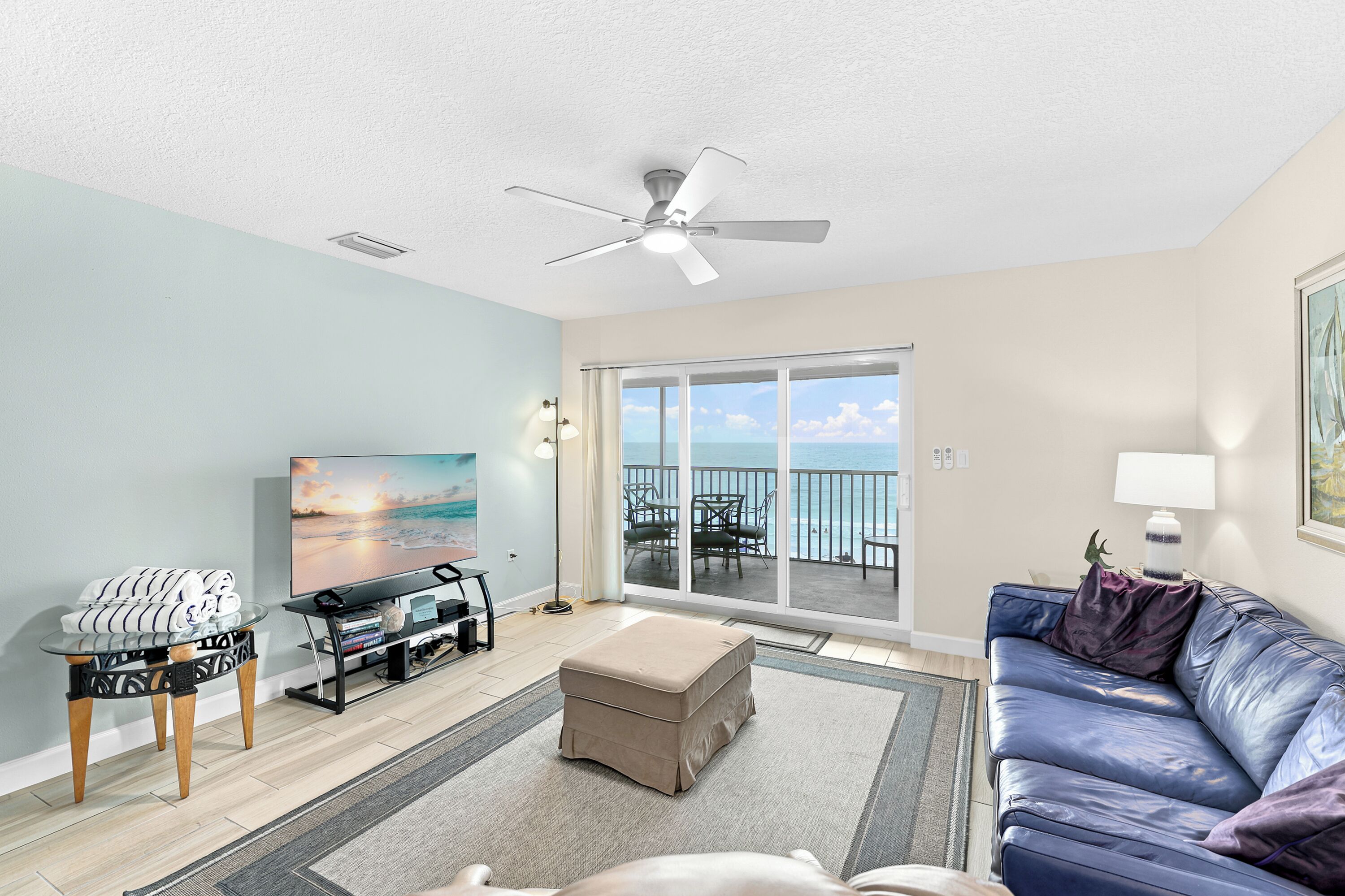 A living room with a television, a sofa, a coffee table, and a view of the ocean through a sliding glass door.