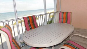 Un balcón con una mesa redonda y cojines a rayas, con vista a una playa y al océano.