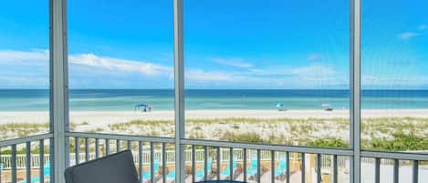 A balcony with a view of a beach, featuring a glass table and chairs.