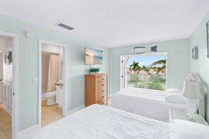 Een slaapkamer met twee bedden, een badkamer en uitzicht op palmbomen en een strand.