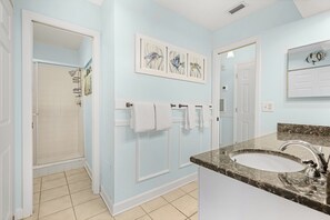 Een badkamer met een douche, een wastafel met een granieten aanrechtblad en kunst aan de muur.