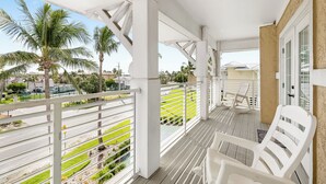 A covered balcony with white railings, white plastic chairs, and a view of a green lawn and palm trees. - Welcome to paradise! Direct beach access, summer and fall dates available!! (Bradenton Beach)