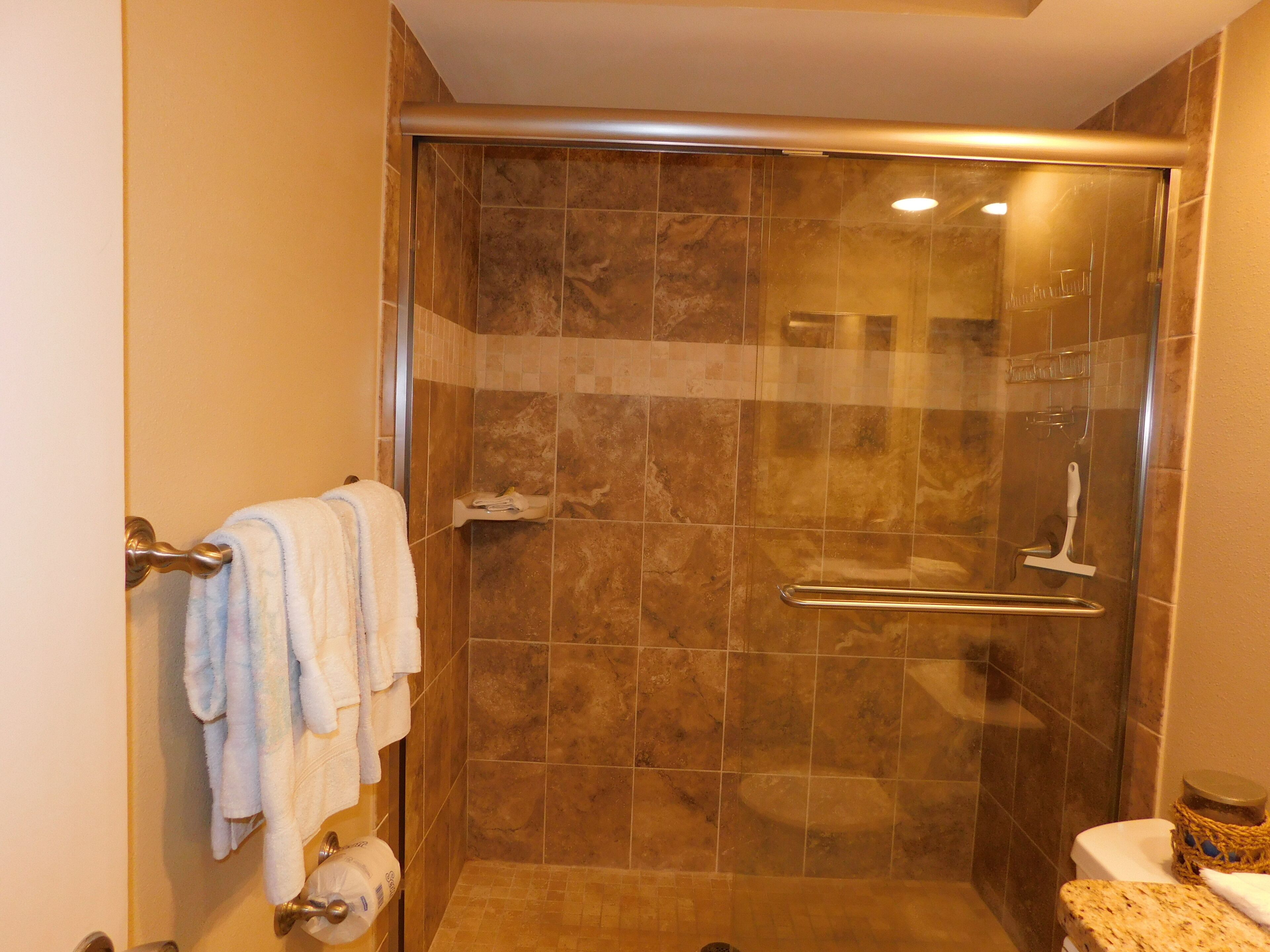 A glass-enclosed shower with a handrail, a toilet, and a towel rack with towels.