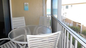 A balcony with a glass table and white chairs, a sign reading "The Ocean Where You Belong", and a view of the ocean and buildings. - Paradise is waiting just for you!  Direct beach access! (Bradenton Beach)
