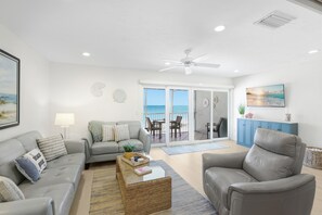 A living room with a sofa, armchair, coffee table, and a view of the ocean through large glass doors.