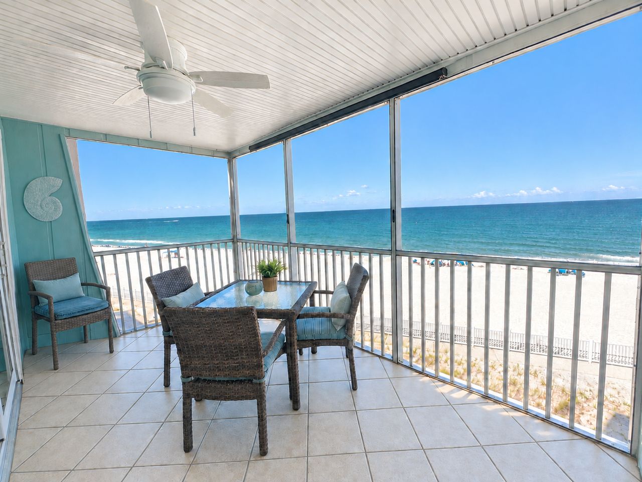 A balcony with a table and chairs, a ceiling fan, and a view of the beach.