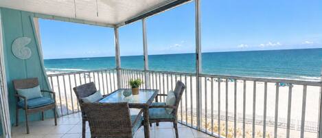 A balcony with a table and chairs, a ceiling fan, and a view of the beach.