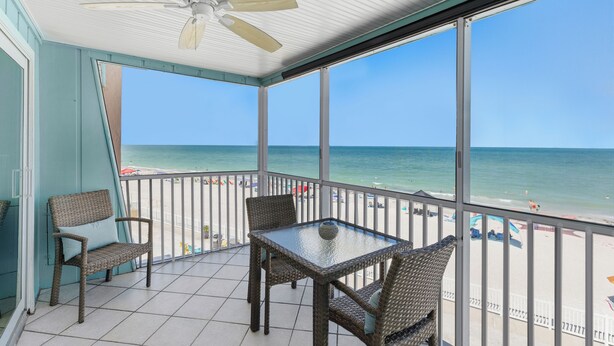 Un balcón techado con mobiliario de mimbre, una mesa y vista a la playa y el océano.