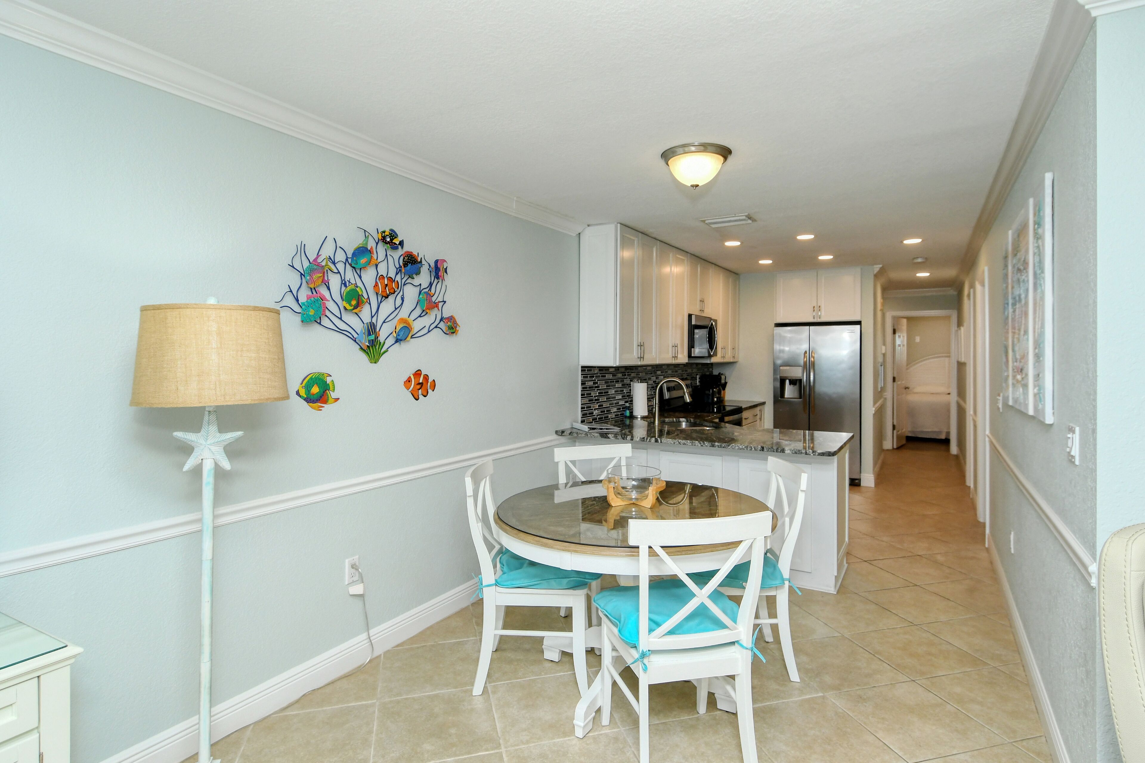 A modern kitchen with white cabinets, a central island, and a dining area with a round table and white chairs.