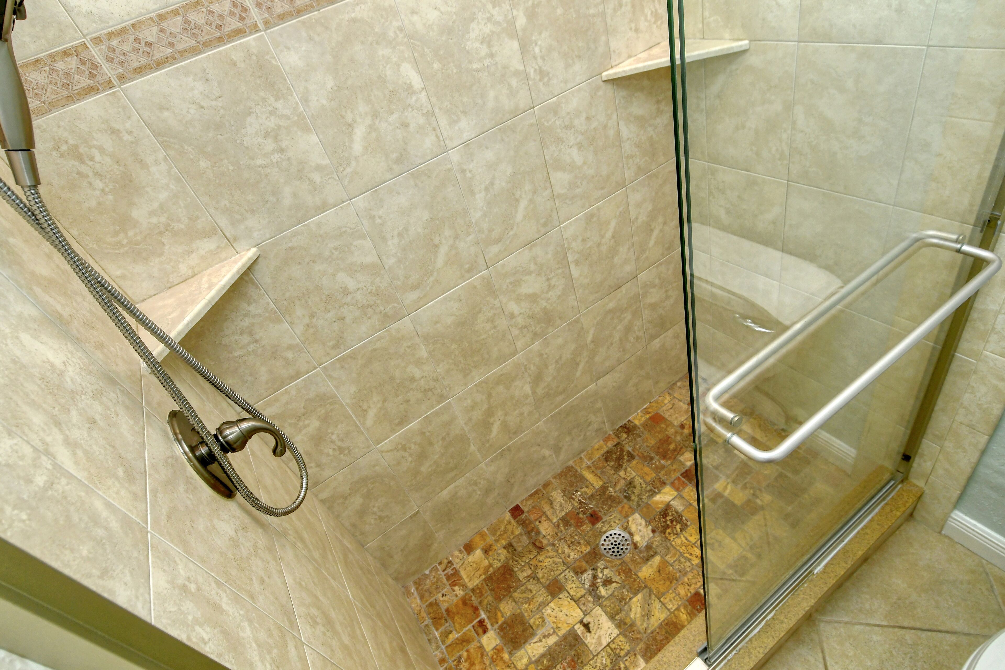 Un espace douche fermé par des parois de verre, avec des carreaux de couleur beige et une pomme de douche.