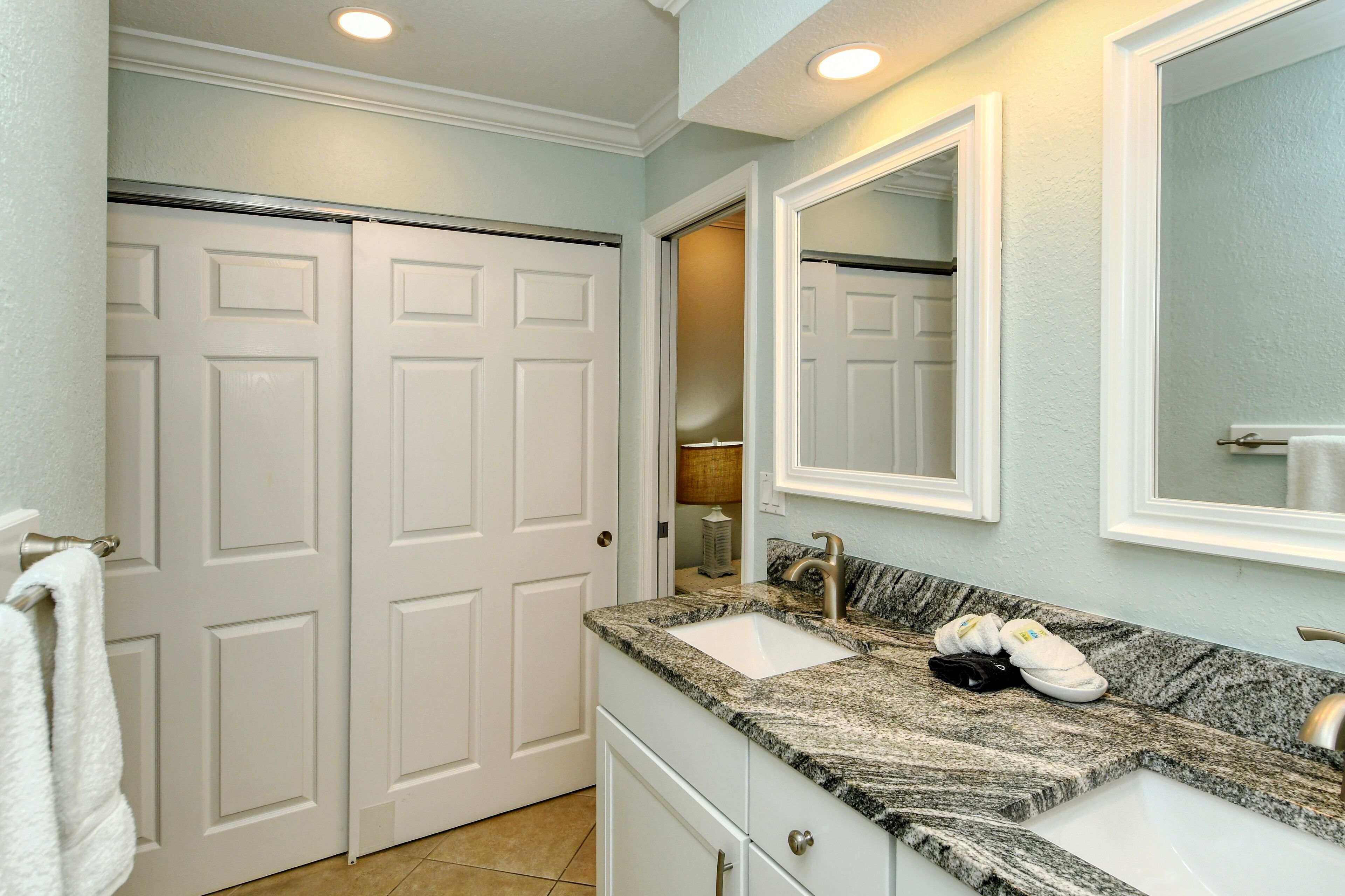 A bathroom with two white doors, a granite countertop, a sink, and a mirror.