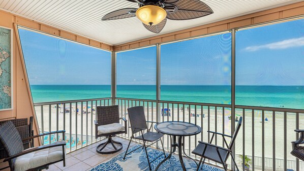 A balcony with a view of the beach, wicker chairs, a table, and a ceiling fan. - Beautiful Gulf View 2/2!! Stunning sunsets every night! (Bradenton Beach)