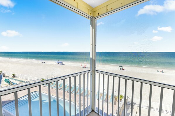 A balcony with a view of a beach and a pool.