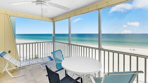 Ein Balkon mit einem weißen Tisch und Stühlen mit Blick auf einen Strand.