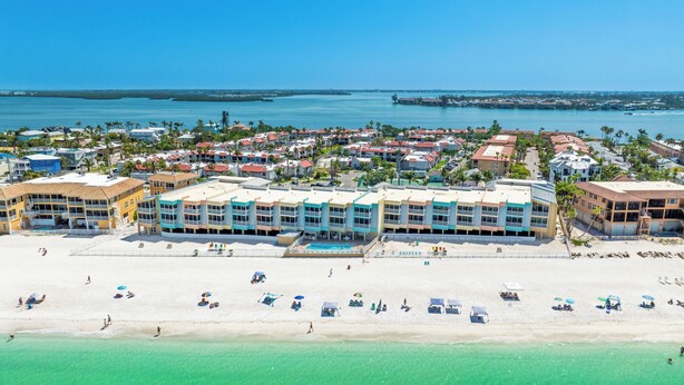 Un hotel frente a la playa con varios balcones, una piscina y una zona de playa con sombrillas.