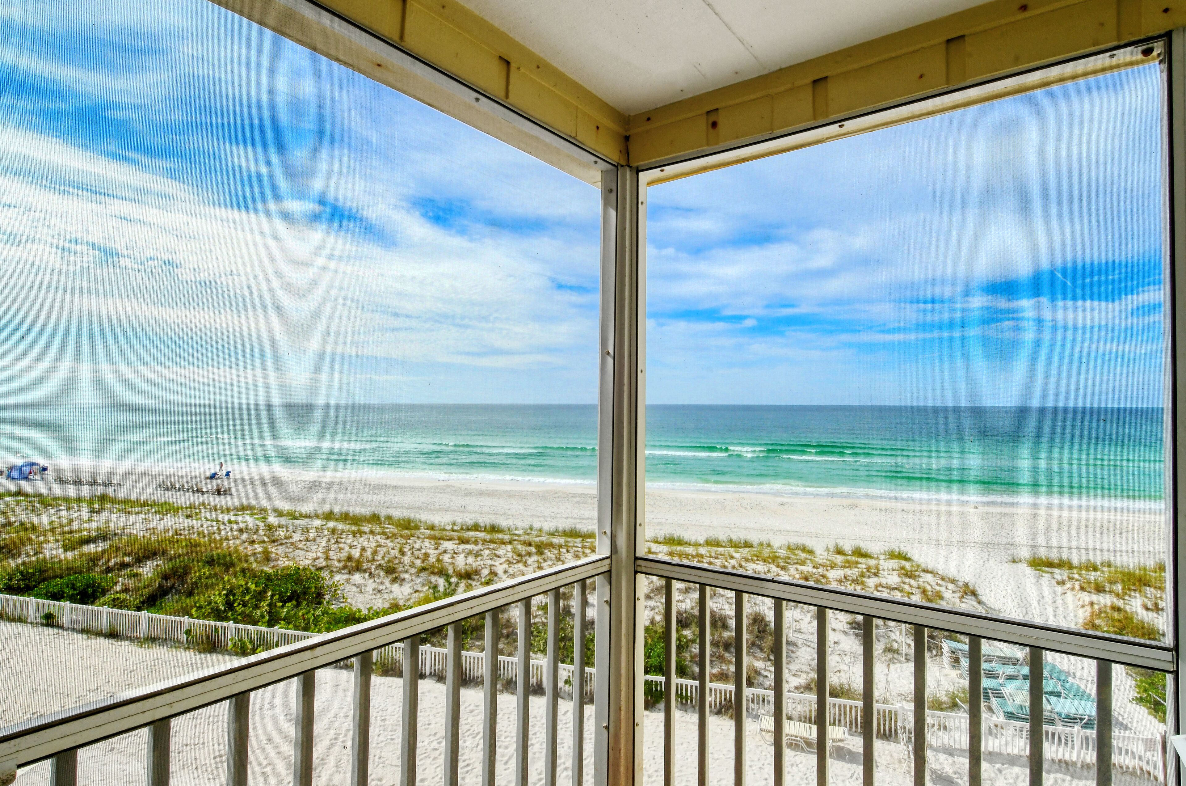A beach view from a balcony with a railing, sandy beach, ocean, and clear sky.