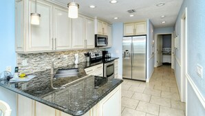 Una cocina moderna con gabinetes blancos, encimeras de granito, electrodomésticos de acero inoxidable y salpicadero de azulejos.