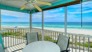 Un espacio al aire libre techado con mesa y sillas, ventilador de techo y vistas a la playa y al océano.