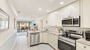Una cocina moderna con armarios blancos, electrodomésticos de acero inoxidable y un amplio ventanal con vistas a un balcón.