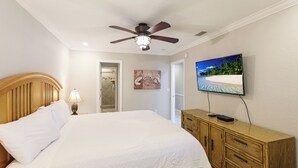 A bedroom with a bed, a ceiling fan, a TV, and a wooden dresser. - Peak a boo Gulf of Mexico balcony views! Direct beach access! Summer and fall dates available! (Bradenton Beach)