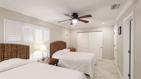 A bedroom with two beds, a ceiling fan, a nightstand with a lamp, and a door.