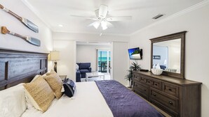 Ein Schlafzimmer mit einem Bett, einem Schminktisch, einem Deckenventilator, einem Fernseher und Blick auf den Balkon.