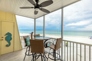 Un balcon abrité, équipé d’une table et de chaises, d’un ventilateur de plafond et offrant une vue sur la plage.