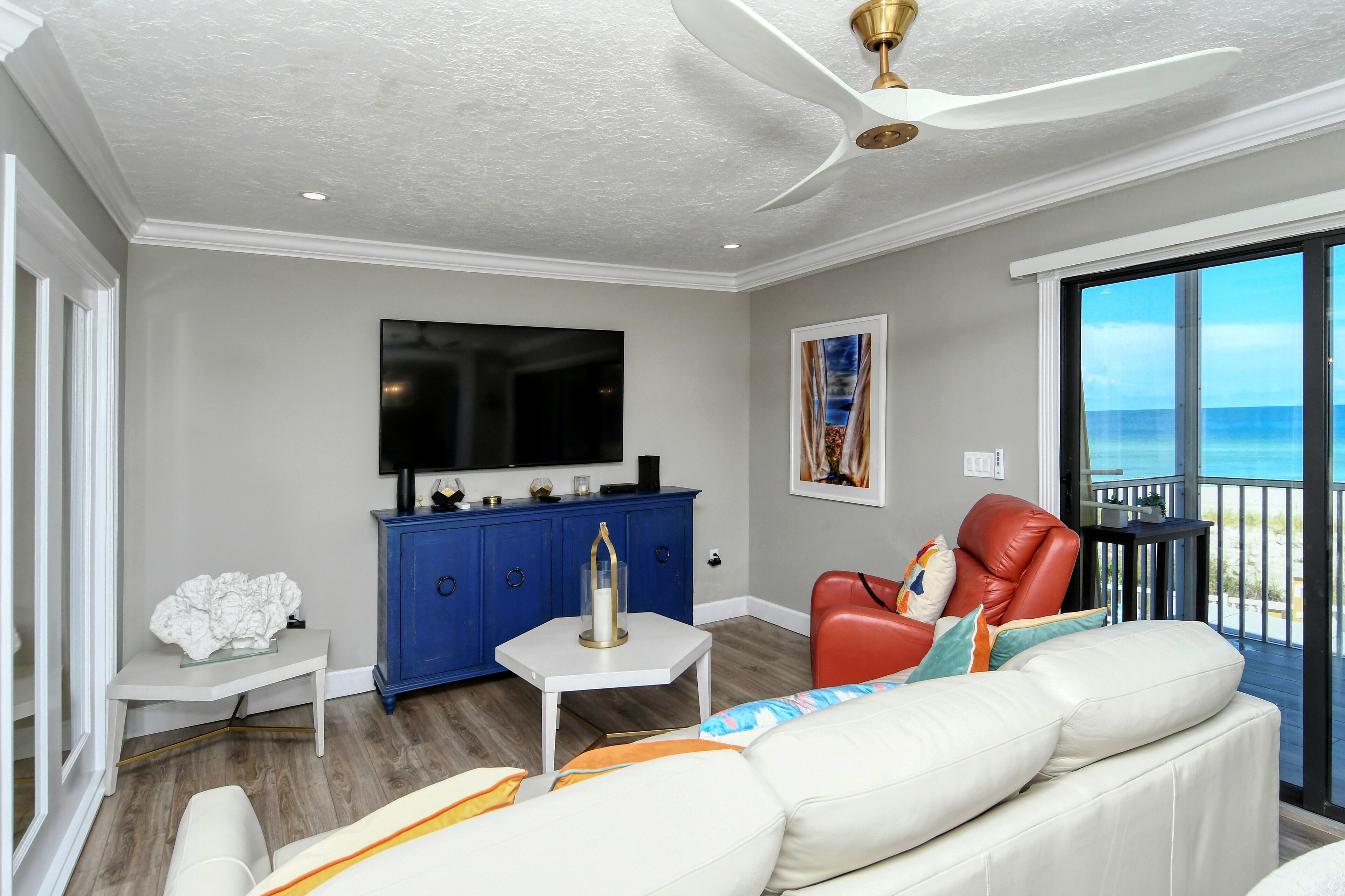 A modern living room with a white sofa, a red chair, a blue cabinet, and a flat-screen TV.