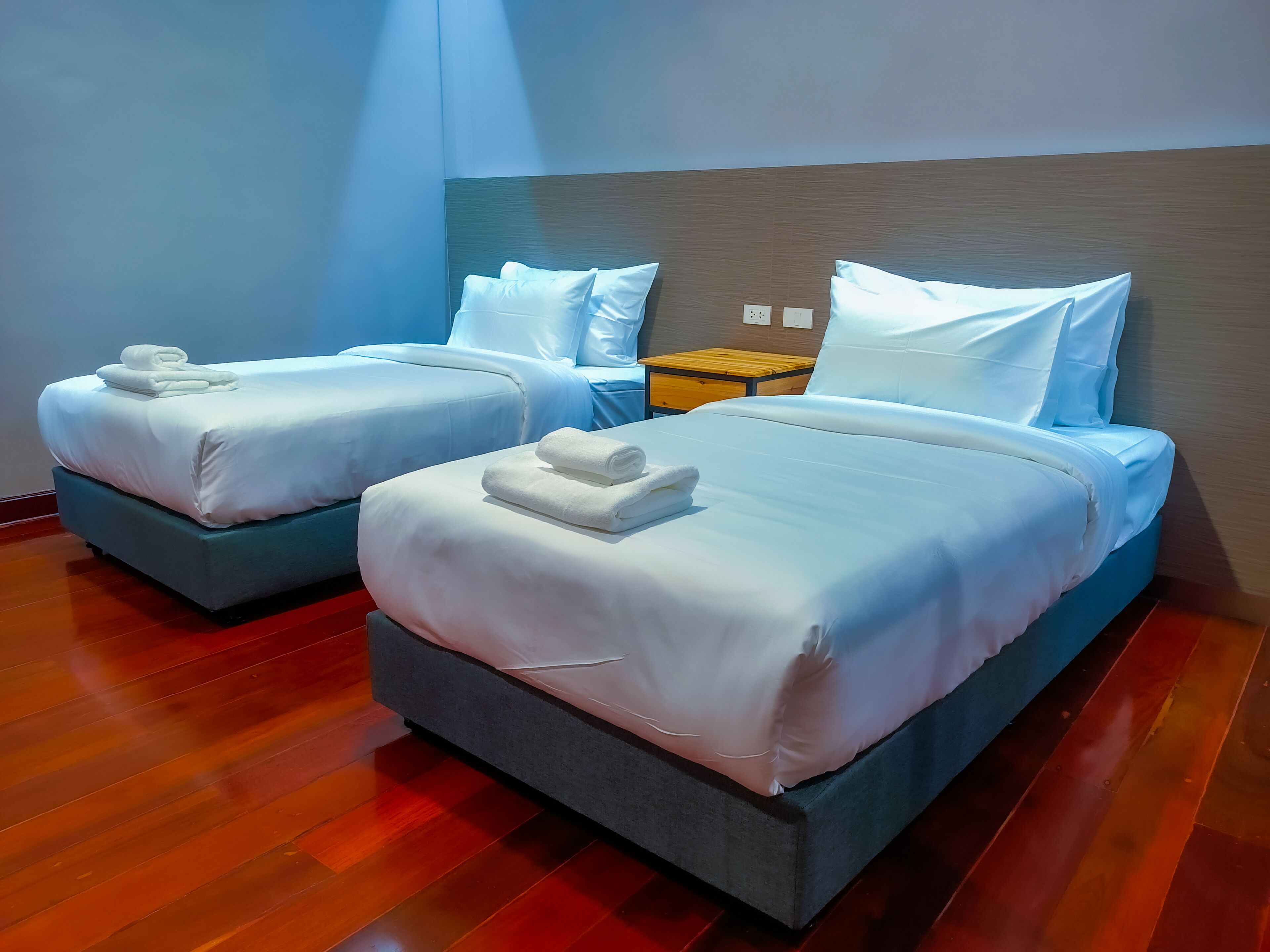 Two single beds with white linens and towels, a wooden nightstand, and a wooden headboard.