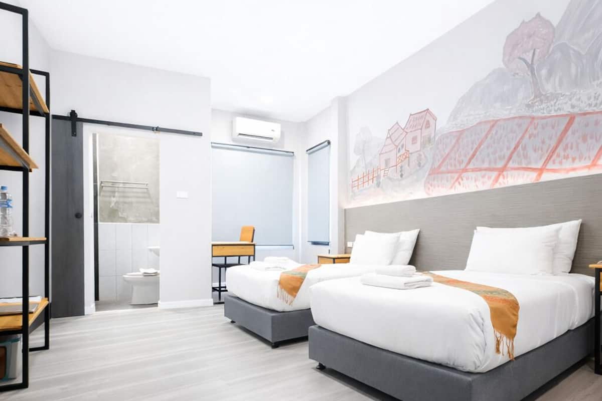 A modern hotel room with two beds, a desk, and a bathroom.