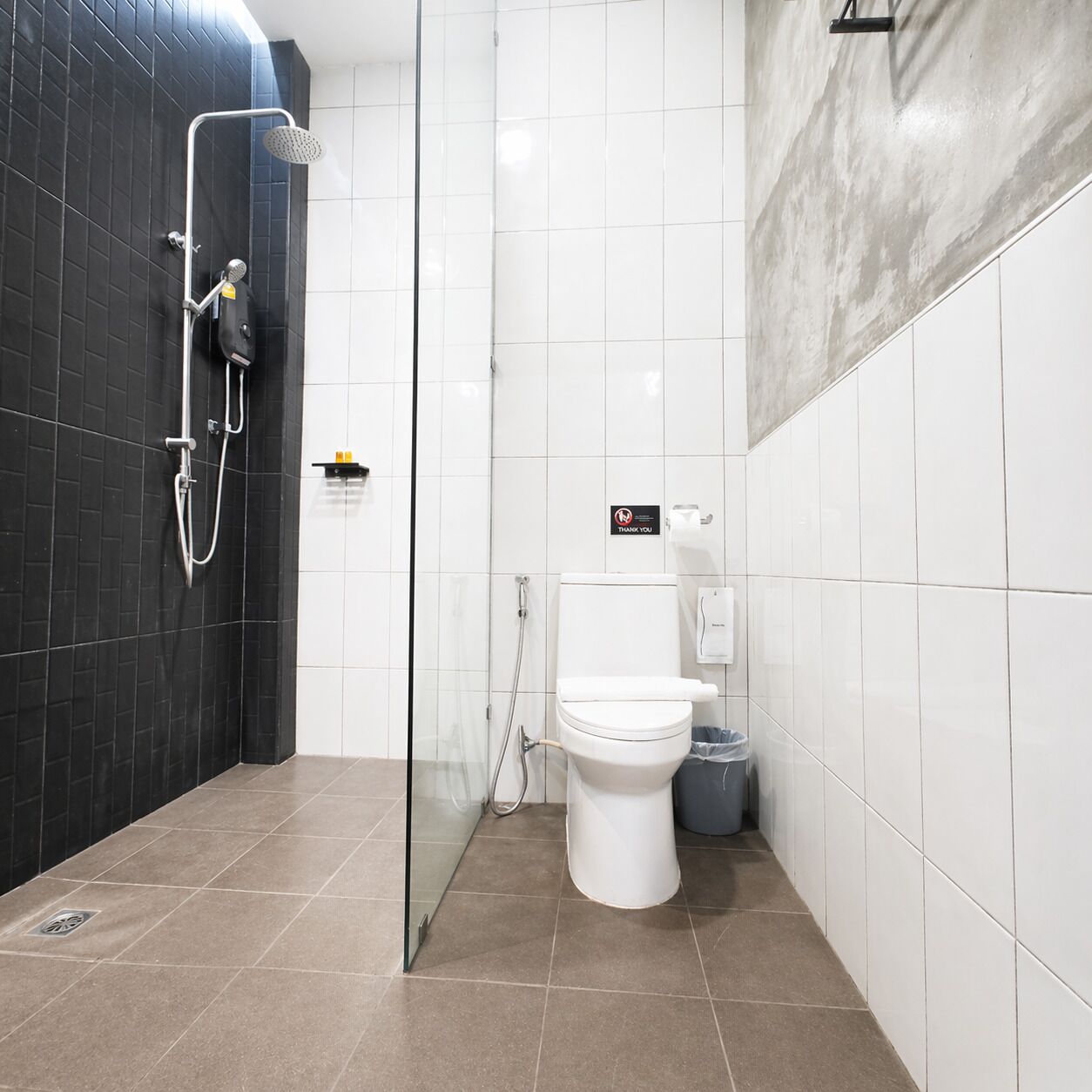 A modern bathroom with a glass shower enclosure, a white toilet, and a trash bin.