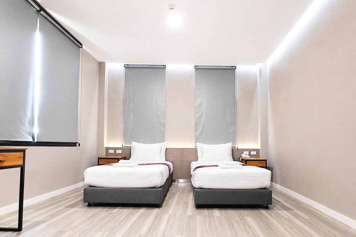 A hotel room with two beds, a desk, a projector screen, and a large window.