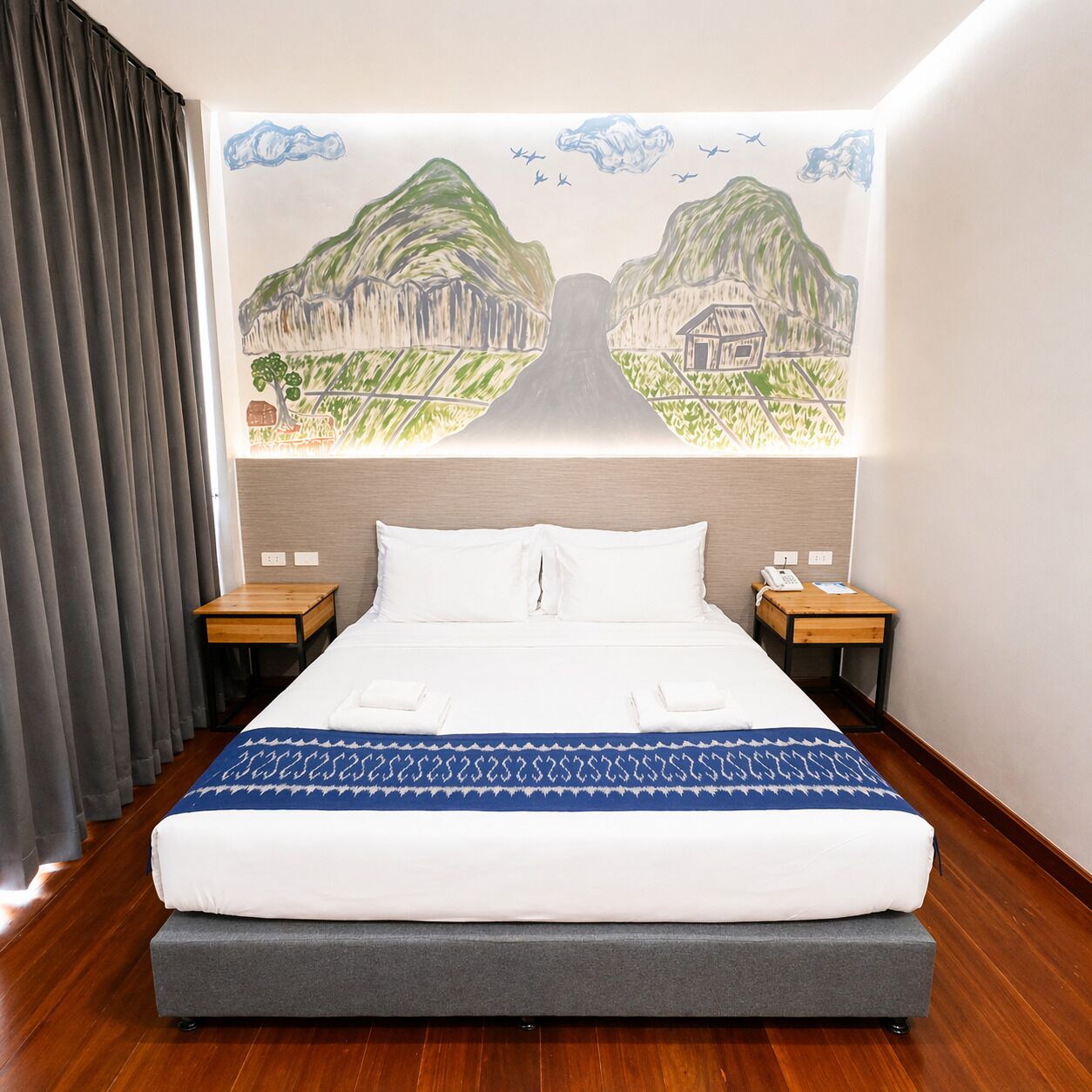 Een hotelkamer met een groot bed, twee nachtkastjes, een hoofdbord met een muurschildering en een houten vloer.